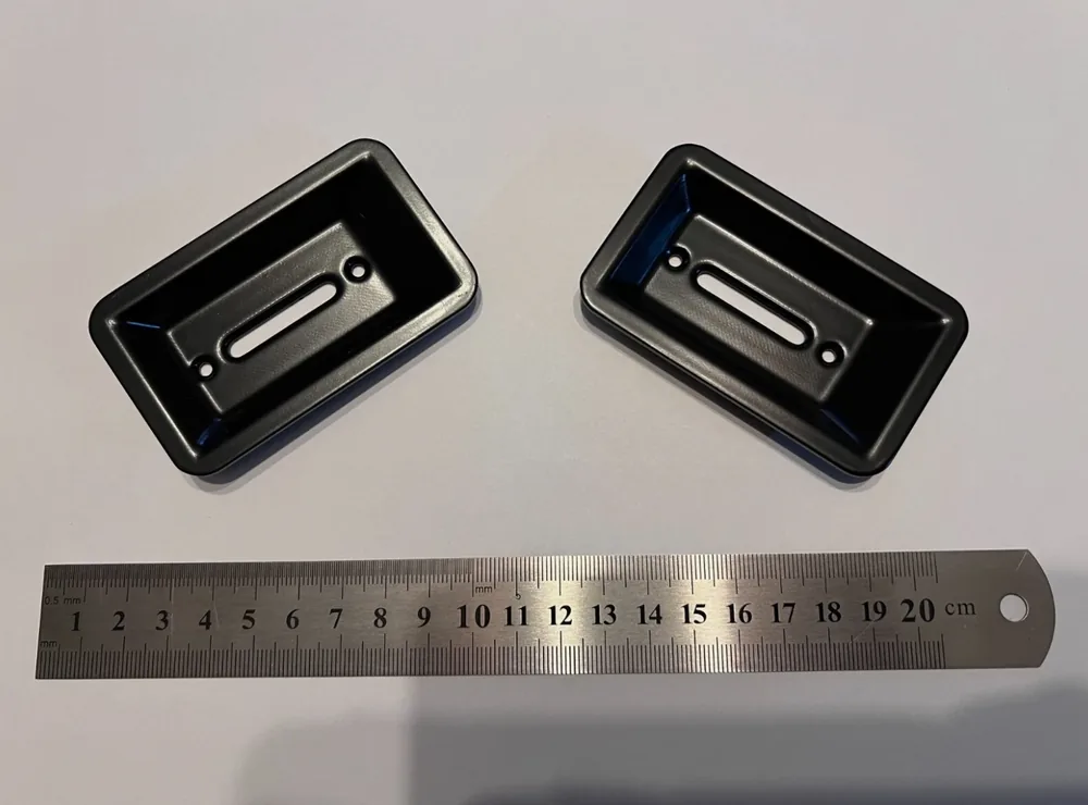 Pair of reproduction Triumph Stag seat bezels in black, beside a ruler